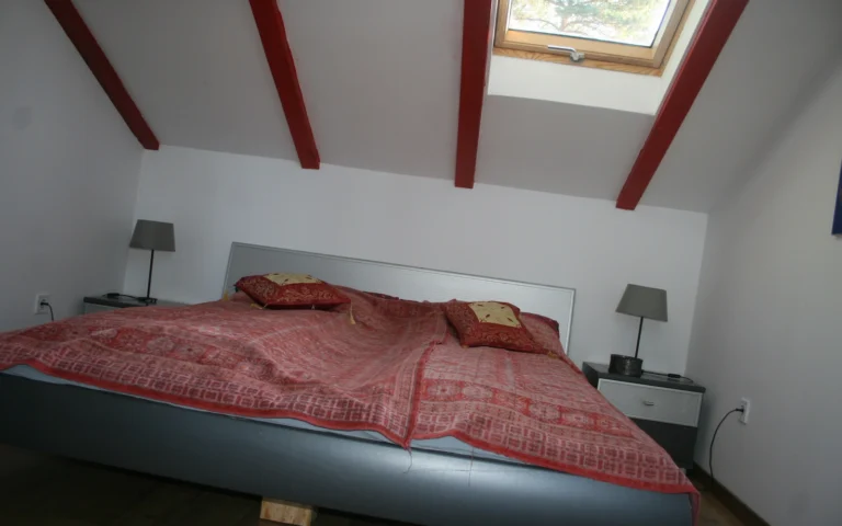 Tetőtéri hálószoba tetőablakkal és látszó gerendákkal a vendégházban